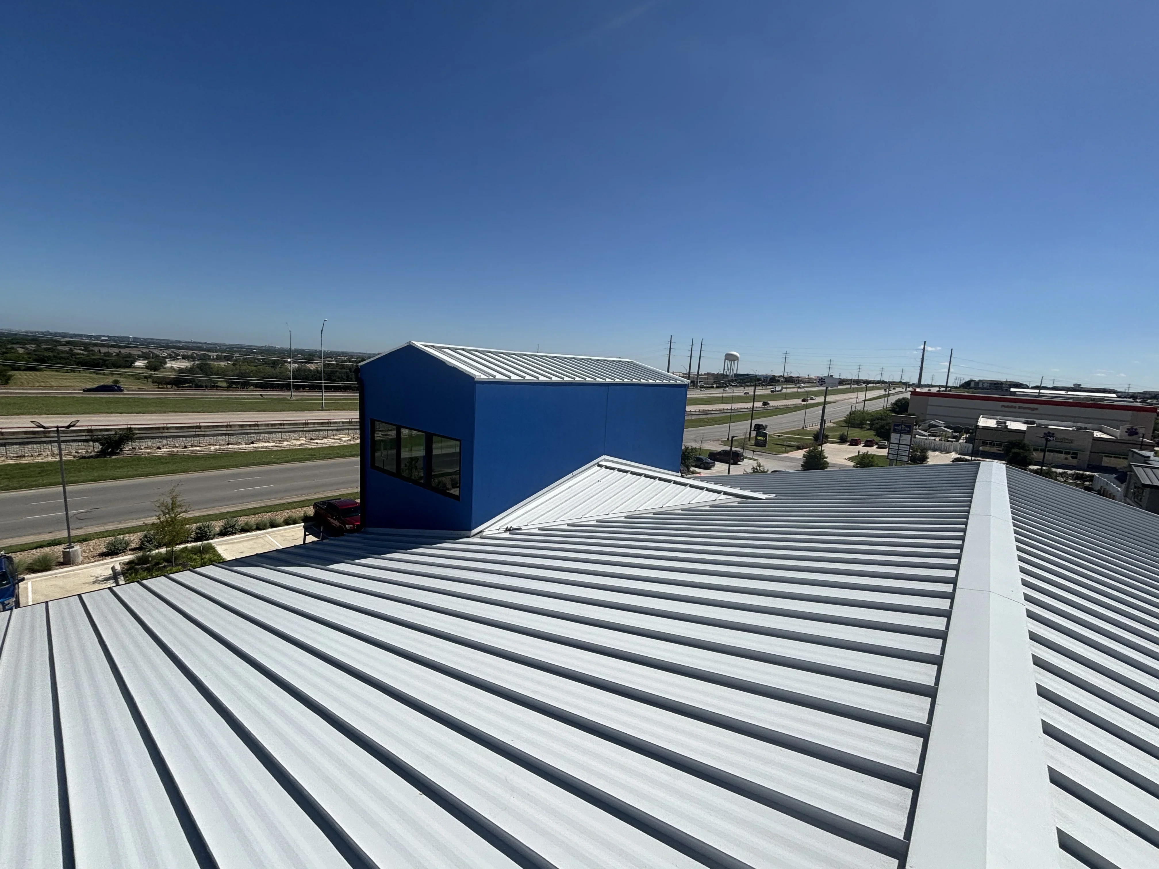 Standing seam metal roof with white and gray panels, blue penthouse structure, commercial installation