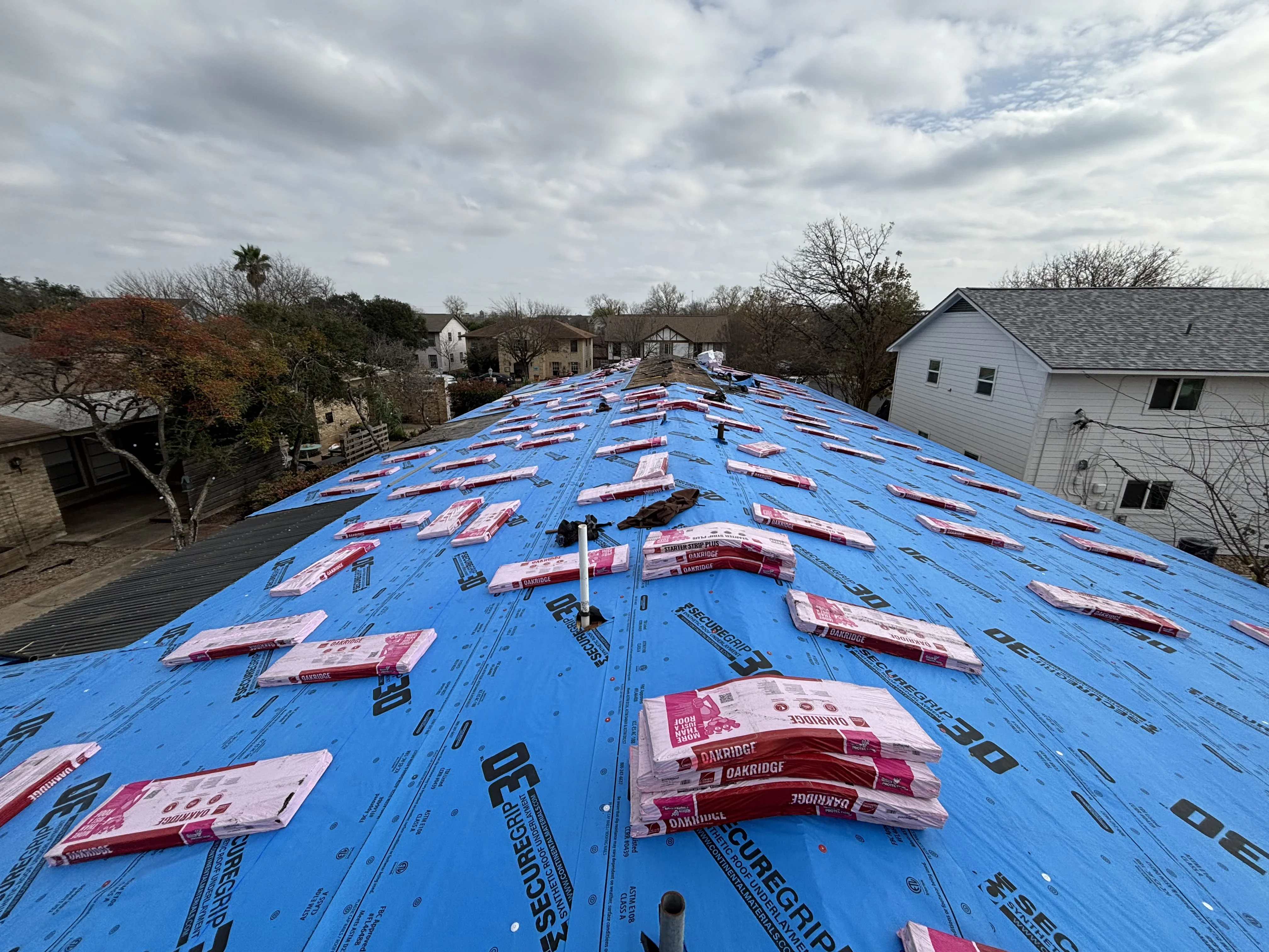 Pitched residential roof with blue underlayment, shingle bundles, and metal flashing during installation