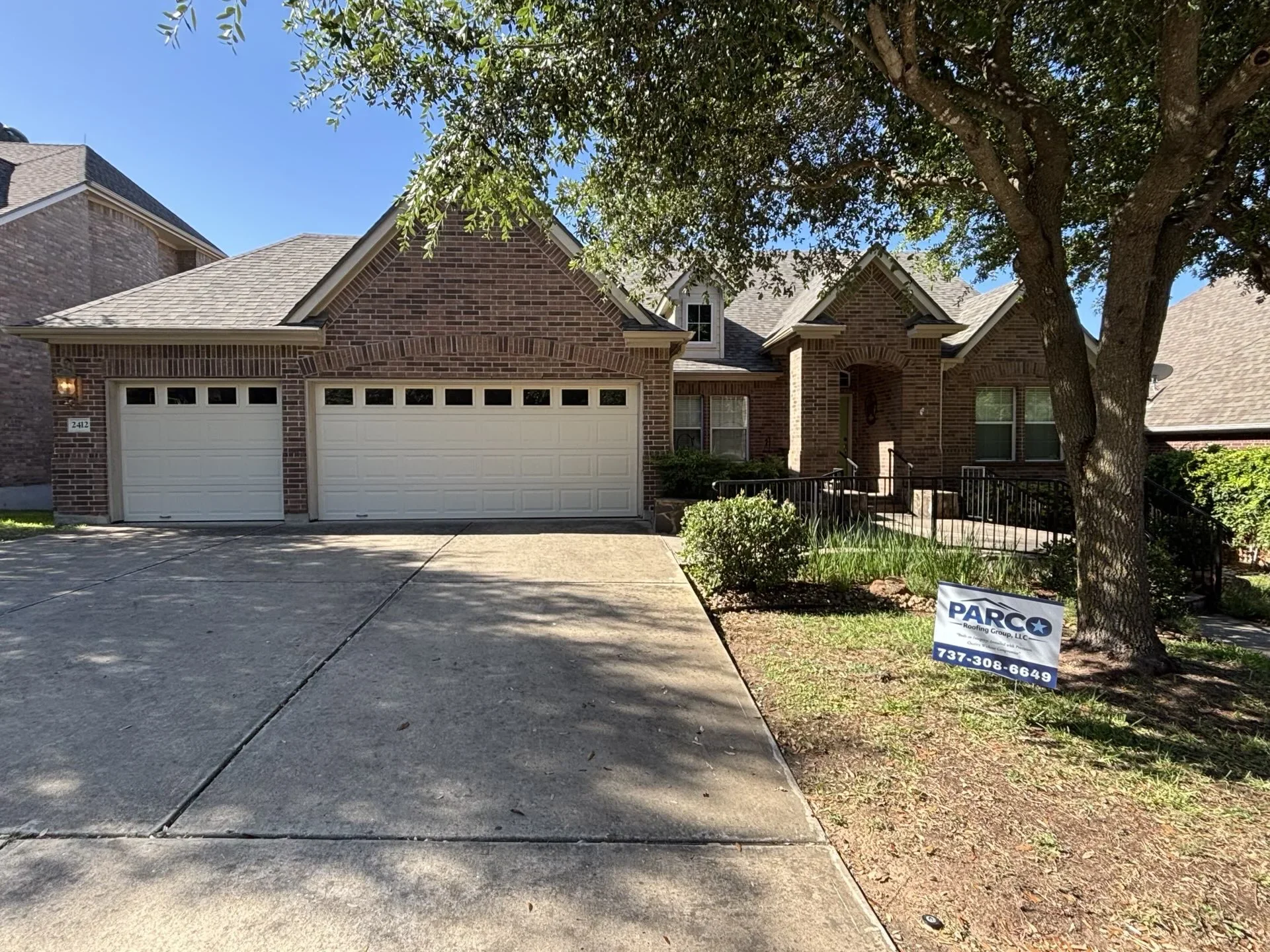 Two-story brick home with new gray architectural shingle roof installation and white garage doors